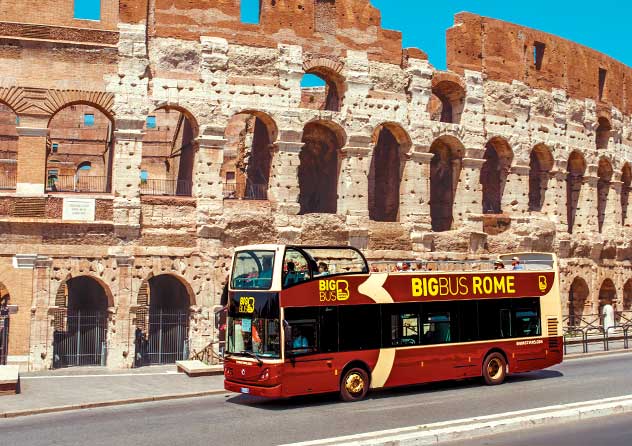 A red Rome city bus stopped at a streetcar stop with historic buildings in the background