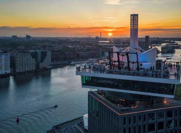Cityscape of Amsterdam illuminated by sunset from a high-rise rooftop bar.