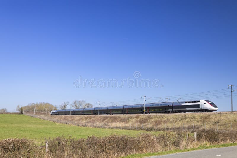 A modern high-speed train speeds past rolling green hills and vineyards in Europe.
