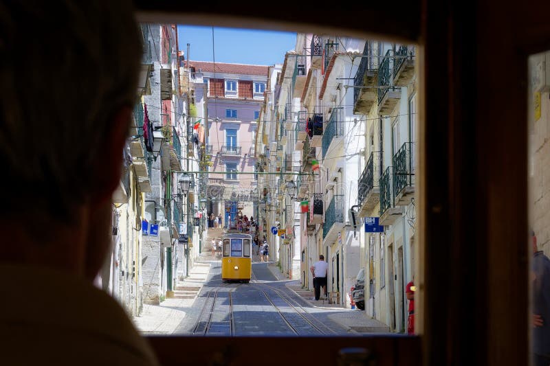 A historic red funicular climbing a steep, cobblestone street in Lisbon