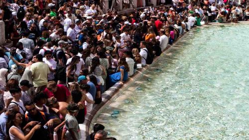 Crowd of people throwing coins into the Trevi Fountain.
