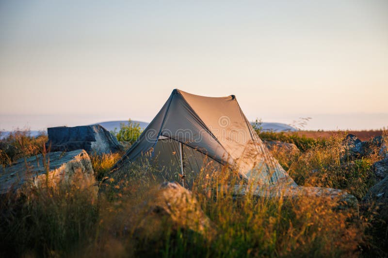 Tents set up on a green campsite with scenic European hills in the background, illustrating affordable outdoor lodging.