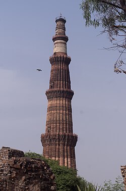 The towering Qutub Minar minaret under a clear blue sky.