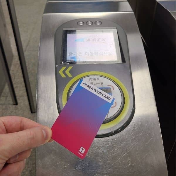 A close-up of a T-Money card being used at a Seoul subway station fare gate.