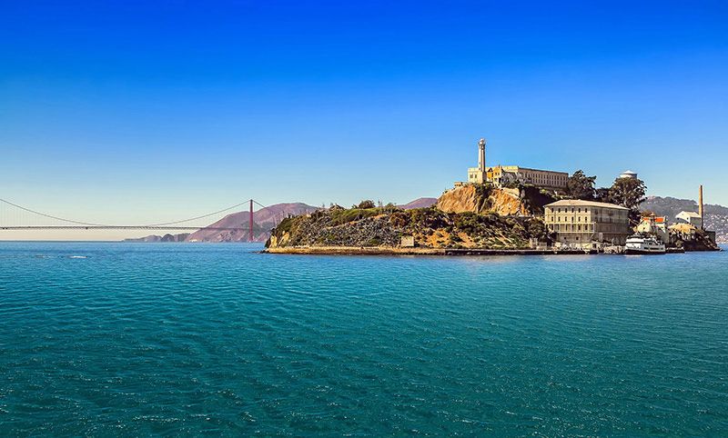 A ferryboat sailing across the bay towards Alcatraz Island with the Golden Gate Bridge visible