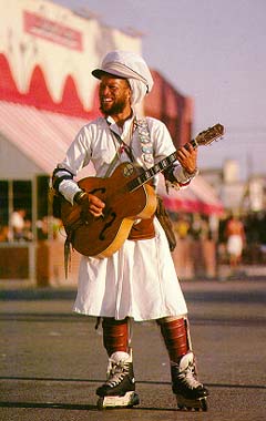 A bustling scene on the Venice Beach Boardwalk with diverse street performers.