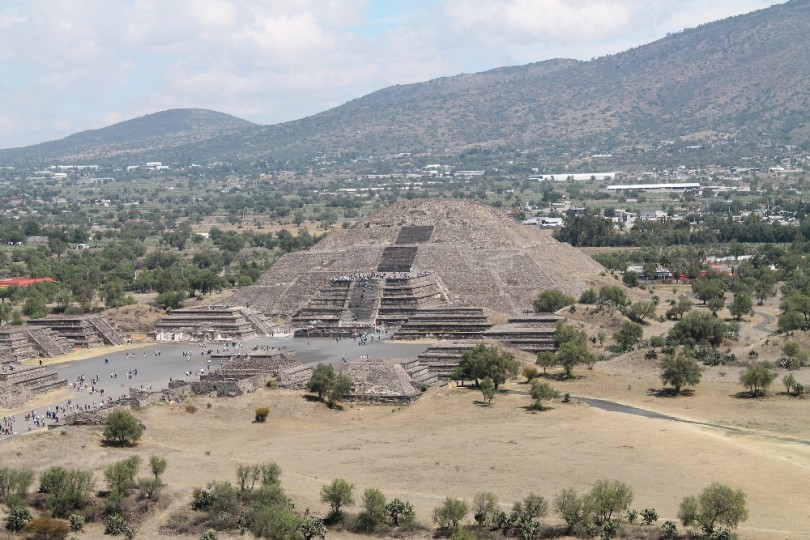 Tourists ascending the historic Pyramid of the Sun at the Teotihuacan archaeological site, with panoramic views in the background.